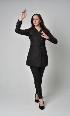 uzun, siyah ceket, gri studio arka plan üzerinde ayakta poz giyen bir esmer kız portresi tam uzunlukta.