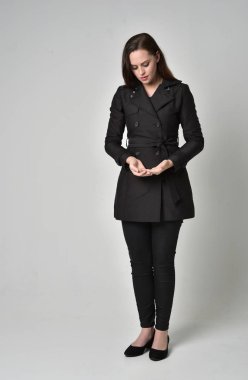 uzun, siyah ceket, gri studio arka plan üzerinde ayakta poz giyen bir esmer kız portresi tam uzunlukta.