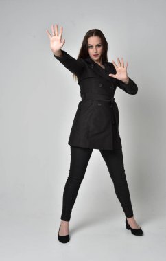 uzun, siyah ceket, gri studio arka plan üzerinde ayakta poz giyen bir esmer kız portresi tam uzunlukta.