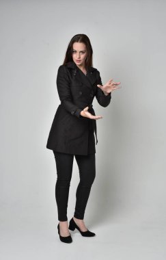 uzun, siyah ceket, gri studio arka plan üzerinde ayakta poz giyen bir esmer kız portresi tam uzunlukta.