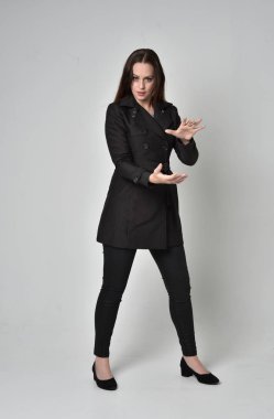 uzun, siyah ceket, gri studio arka plan üzerinde ayakta poz giyen bir esmer kız portresi tam uzunlukta.