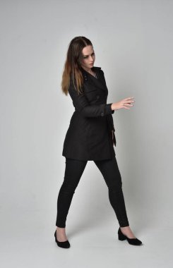 uzun, siyah ceket, gri studio arka plan üzerinde ayakta poz giyen bir esmer kız portresi tam uzunlukta.