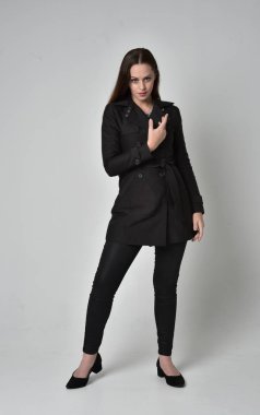 uzun, siyah ceket, gri studio arka plan üzerinde ayakta poz giyen bir esmer kız portresi tam uzunlukta.