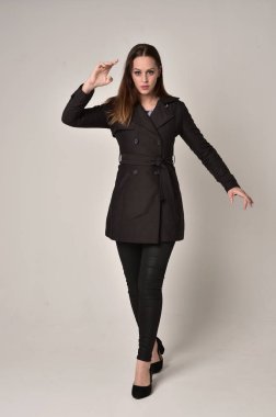 uzun, siyah ceket, gri studio arka plan üzerinde ayakta poz giyen bir esmer kız portresi tam uzunlukta.