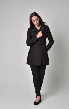 uzun, siyah ceket, gri studio arka plan üzerinde ayakta poz giyen bir esmer kız portresi tam uzunlukta.