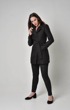 uzun, siyah ceket, gri studio arka plan üzerinde ayakta poz giyen bir esmer kız portresi tam uzunlukta.