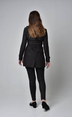 uzun, siyah ceket, gri studio arka plan üzerinde kameranın arka ayakta pozuyla giyen bir esmer kız portresi tam uzunlukta.