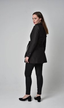 uzun, siyah ceket, gri studio arka plan üzerinde kameranın arka ayakta pozuyla giyen bir esmer kız portresi tam uzunlukta.