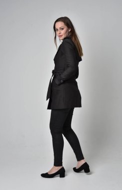 uzun, siyah ceket, gri studio arka plan üzerinde kameranın arka ayakta pozuyla giyen bir esmer kız portresi tam uzunlukta.