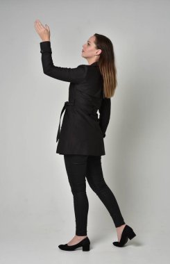 uzun, siyah ceket, gri studio arka plan üzerinde kameranın arka ayakta pozuyla giyen bir esmer kız portresi tam uzunlukta.