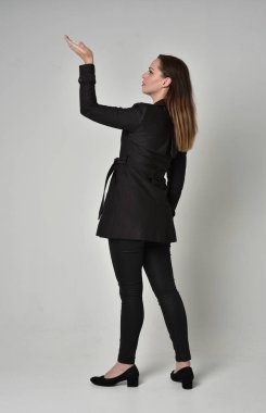 uzun, siyah ceket, gri studio arka plan üzerinde kameranın arka ayakta pozuyla giyen bir esmer kız portresi tam uzunlukta.