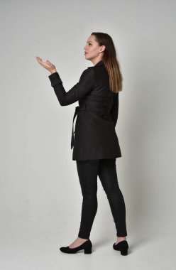 uzun, siyah ceket, gri studio arka plan üzerinde kameranın arka ayakta pozuyla giyen bir esmer kız portresi tam uzunlukta.