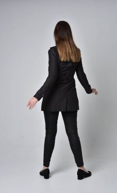 uzun, siyah ceket, gri studio arka plan üzerinde kameranın arka ayakta pozuyla giyen bir esmer kız portresi tam uzunlukta.