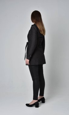 uzun, siyah ceket, gri studio arka plan üzerinde kameranın arka ayakta pozuyla giyen bir esmer kız portresi tam uzunlukta.