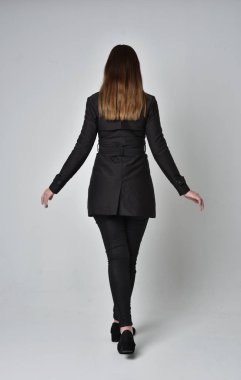 uzun, siyah ceket, gri studio arka plan üzerinde kameranın arka ayakta pozuyla giyen bir esmer kız portresi tam uzunlukta.