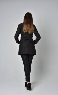 uzun, siyah ceket, gri studio arka plan üzerinde kameranın arka ayakta pozuyla giyen bir esmer kız portresi tam uzunlukta.