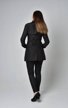 uzun, siyah ceket, gri studio arka plan üzerinde kameranın arka ayakta pozuyla giyen bir esmer kız portresi tam uzunlukta.