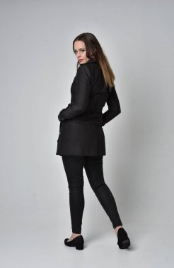 uzun, siyah ceket, gri studio arka plan üzerinde kameranın arka ayakta pozuyla giyen bir esmer kız portresi tam uzunlukta.