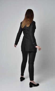 uzun, siyah ceket, gri studio arka plan üzerinde kameranın arka ayakta pozuyla giyen bir esmer kız portresi tam uzunlukta.