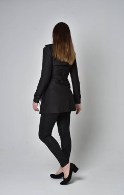 uzun, siyah ceket, gri studio arka plan üzerinde kameranın arka ayakta pozuyla giyen bir esmer kız portresi tam uzunlukta.