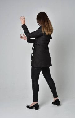 uzun, siyah ceket, gri studio arka plan üzerinde kameranın arka ayakta pozuyla giyen bir esmer kız portresi tam uzunlukta.