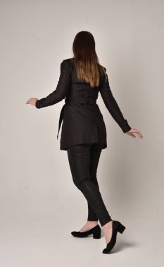 uzun, siyah ceket, gri studio arka plan üzerinde kameranın arka ayakta pozuyla giyen bir esmer kız portresi tam uzunlukta.