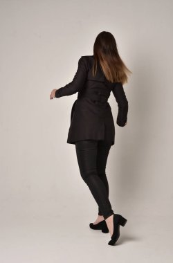 uzun, siyah ceket, gri studio arka plan üzerinde kameranın arka ayakta pozuyla giyen bir esmer kız portresi tam uzunlukta.