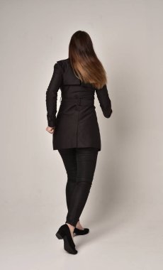 uzun, siyah ceket, gri studio arka plan üzerinde kameranın arka ayakta pozuyla giyen bir esmer kız portresi tam uzunlukta.