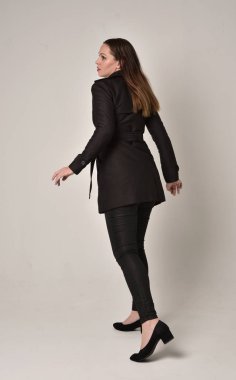 uzun, siyah ceket, gri studio arka plan üzerinde kameranın arka ayakta pozuyla giyen bir esmer kız portresi tam uzunlukta.
