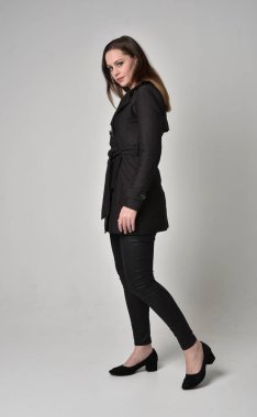 uzun, siyah ceket, gri studio arka plan üzerinde yan profil ayakta poz giyen bir esmer kız portresi tam uzunlukta.