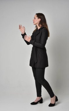 uzun, siyah ceket, gri studio arka plan üzerinde yan profil ayakta poz giyen bir esmer kız portresi tam uzunlukta.