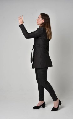 uzun, siyah ceket, gri studio arka plan üzerinde yan profil ayakta poz giyen bir esmer kız portresi tam uzunlukta.