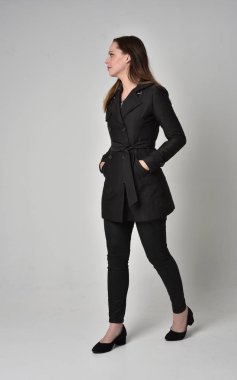 uzun, siyah ceket, gri studio arka plan üzerinde yan profil ayakta poz giyen bir esmer kız portresi tam uzunlukta.