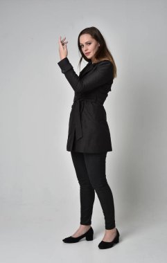 uzun, siyah ceket, gri studio arka plan üzerinde yan profil ayakta poz giyen bir esmer kız portresi tam uzunlukta.