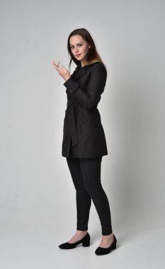 uzun, siyah ceket, gri studio arka plan üzerinde yan profil ayakta poz giyen bir esmer kız portresi tam uzunlukta.