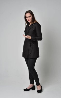 uzun, siyah ceket, gri studio arka plan üzerinde yan profil ayakta poz giyen bir esmer kız portresi tam uzunlukta.