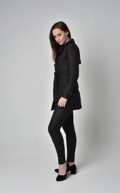 uzun, siyah ceket, gri studio arka plan üzerinde yan profil ayakta poz giyen bir esmer kız portresi tam uzunlukta.