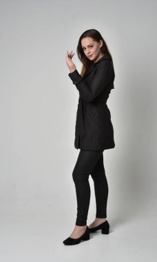 uzun, siyah ceket, gri studio arka plan üzerinde yan profil ayakta poz giyen bir esmer kız portresi tam uzunlukta.