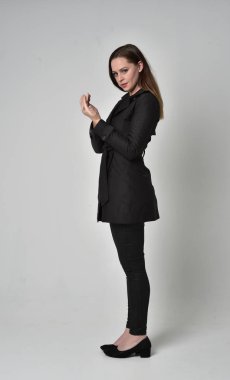 uzun, siyah ceket, gri studio arka plan üzerinde yan profil ayakta poz giyen bir esmer kız portresi tam uzunlukta.