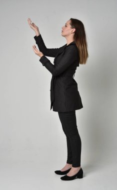 uzun, siyah ceket, gri studio arka plan üzerinde yan profil ayakta poz giyen bir esmer kız portresi tam uzunlukta.