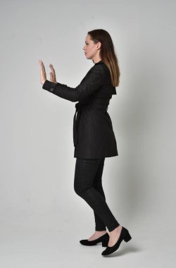 uzun, siyah ceket, gri studio arka plan üzerinde yan profil ayakta poz giyen bir esmer kız portresi tam uzunlukta.