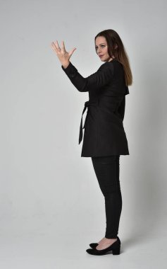 uzun, siyah ceket, gri studio arka plan üzerinde yan profil ayakta poz giyen bir esmer kız portresi tam uzunlukta.