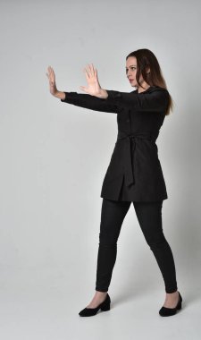 uzun, siyah ceket, gri studio arka plan üzerinde yan profil ayakta poz giyen bir esmer kız portresi tam uzunlukta.