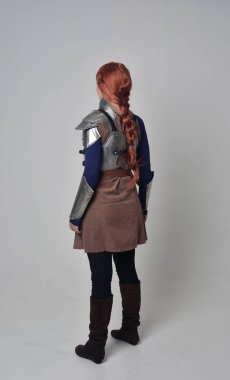 Ortaçağ savaşçı kostüm ve çelik zırh, kameranın arkasında gri studio arka plan ayakta pozuyla giyen bir kırmızı saçlı kız portresi tam uzunlukta.