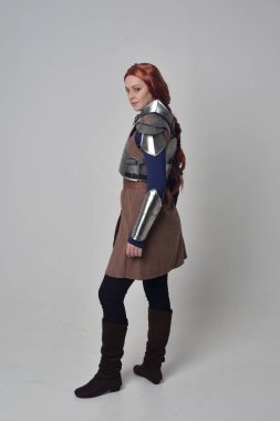 Ortaçağ savaşçı kostüm ve çelik zırh, kameranın arkasında gri studio arka plan ayakta pozuyla giyen bir kırmızı saçlı kız portresi tam uzunlukta.