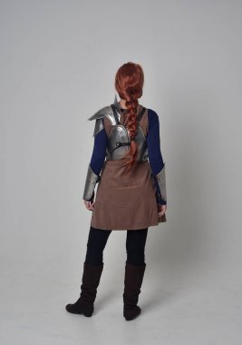 Ortaçağ savaşçı kostüm ve çelik zırh, kameranın arkasında gri studio arka plan ayakta pozuyla giyen bir kırmızı saçlı kız portresi tam uzunlukta.