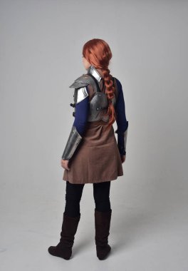 Ortaçağ savaşçı kostüm ve çelik zırh, kameranın arkasında gri studio arka plan ayakta pozuyla giyen bir kırmızı saçlı kız portresi tam uzunlukta.