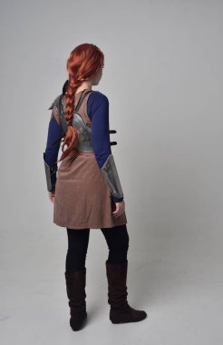 Ortaçağ savaşçı kostüm ve çelik zırh, kameranın arkasında gri studio arka plan ayakta pozuyla giyen bir kırmızı saçlı kız portresi tam uzunlukta.