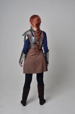 Ortaçağ savaşçı kostüm ve çelik zırh, kameranın arkasında gri studio arka plan ayakta pozuyla giyen bir kırmızı saçlı kız portresi tam uzunlukta.