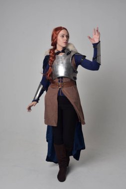 Ortaçağ savaşçı kostüm, mavi kadife pelerin ve çelik zırh, ayakta poz gri studio arka plan üzerinde kırmızı saçlı kız portresi tam uzunlukta.